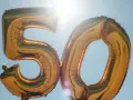Gyllene ballonger formar siffran 50 mot en klarblå himmel. Perfekt för roliga frågor till 50 års fest!