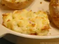 En närbild på en krämig, osttäckt bakad potatis fylld med baconbitar.