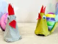 Två påskkycklingar gjorda av äggkartonger, med färgglada ägg och fjädrar. Ett roligt pyssel för påsk barn.