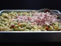 Stor ugnsform fylld med pastasallad med kassler, grönsaker och en sked.