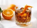 En drink med is och apelsinskal, bredvid färska apelsiner. Perfekt för ett sockerlag recept.