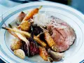 En tallrik med skivad rostbiff, rostade rotfrukter som morötter och palsternacka, samt vitlök. Ett perfekt rostbiff recept för en festmåltid.