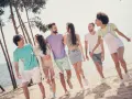 En grupp glada vänner på stranden, en riktig tipspromenad med twist. De skrattar och går längs vattnet bland tallar.