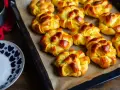 Nybakade lussebullar med kesella, gyllene och redo att avnjutas. En skål med socker och en röd duk anas i bakgrunden.