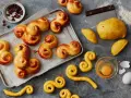 En bricka med gyllene, nybakade lussekatterna, redo att avnjutas. Bredvid ligger ingredienser som russin, deg och ett ägg. Dessa är de godaste lussekatterna!