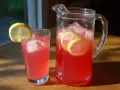 En karaff och ett glas med rosa rabarbersaft, is och citronskivor. Perfekt för ett enkelt rabarbersaft recept.