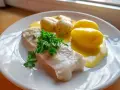 En portion rimmad torsk med kokt potatis och en krämig sås, garnerad med färsk persilja.