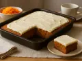 En saftig morotskaka i långpanna med krämig frosting. En bit är upplagd på en tallrik, redo att avnjutas.