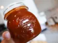 En hand håller ett glas med en mörkröd rabarber chutney.