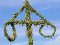 En midsommarstång, dekorerad med grönska och blommor, mot en blå himmel. En symbol för sommar och glädje, en viktig del av fakta om midsommar.