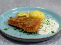 Panerad fisk med kokt potatis, ärtor och en krämig kall sås till fisk, garnerad med gräslök och citronklyftor.