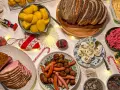 Julbord med jullekar vid bordet: skinka, köttbullar, prinskorv, sill, ägg och bröd. Julpynt och ljusslingor skapar stämning.