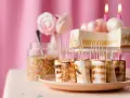 Rostade marshmallows på spett, perfekt för roliga recept att baka till kalaset. En burk strössel och en tårta i bakgrunden.