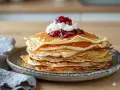En hög med fluffiga svenska pannkakor toppas med vispad grädde och sylt. Perfekt för en mysig fika.