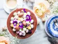 En chokladtårta dekorerad med påskägg i olika färger och violer. En perfekt påsktårta choklad för firandet.
