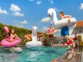 Ungdomar hoppar i poolen med uppblåsbara badleksaker som flamingo, enhörning och bajskorv. Perfekt för midsommarlekar inomhus eller utomhus!