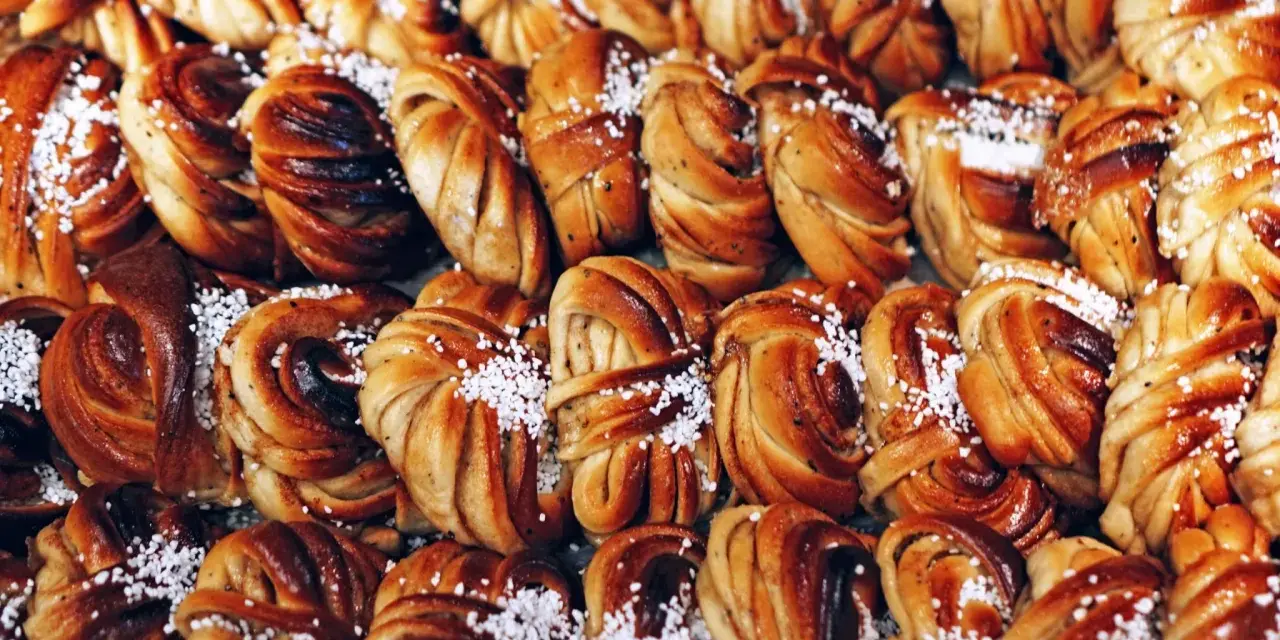 En stor hög med gyllene kanelbullar, perfekta för kanelbullens dag. Strösslade med pärlsocker.