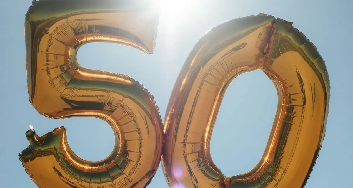 Gyllene ballonger formar siffran 50 mot en klarblå himmel. Perfekt för roliga frågor till 50 års fest!