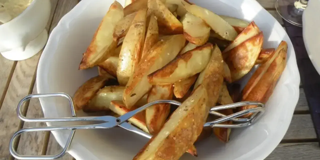 En skål med gyllene klyftpotatis i ugn, redo att serveras med tång.