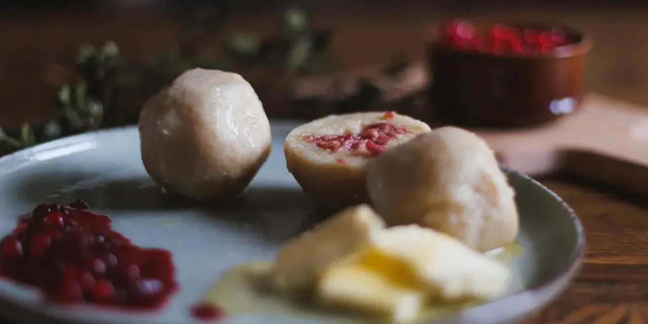 En tallrik med pitepalt, lingonsylt och smör. En halv palt visar en fyllning av fläsk. Perfekt för ett recept på pitepalt.