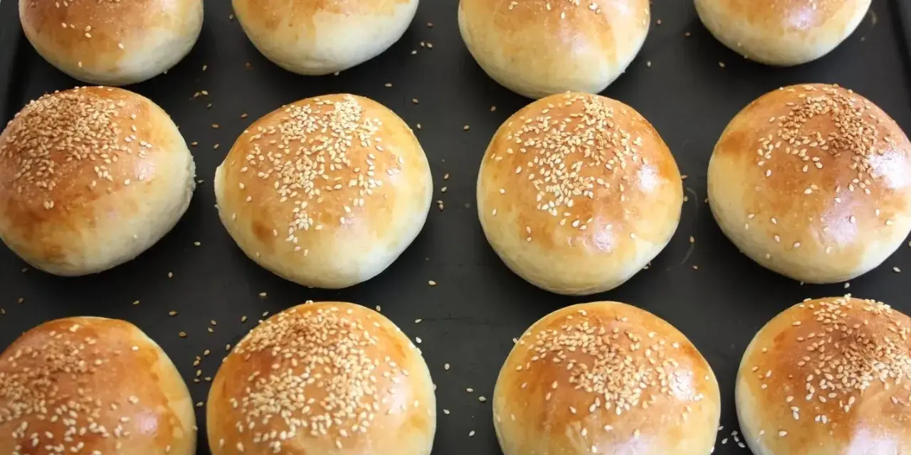 Nybakade frallor med sesamfrön på en plåt, redo att ätas. Perfekt för att baka frallor till frukost eller fika.