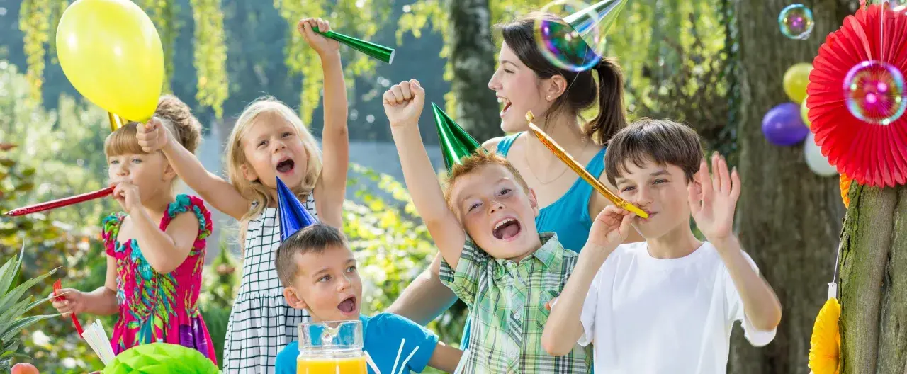 Barn firar ett 7-årskalas utomhus med ballonger, serpentiner och såpbubblor. Glada barn med partyhattar blåser i tutor.