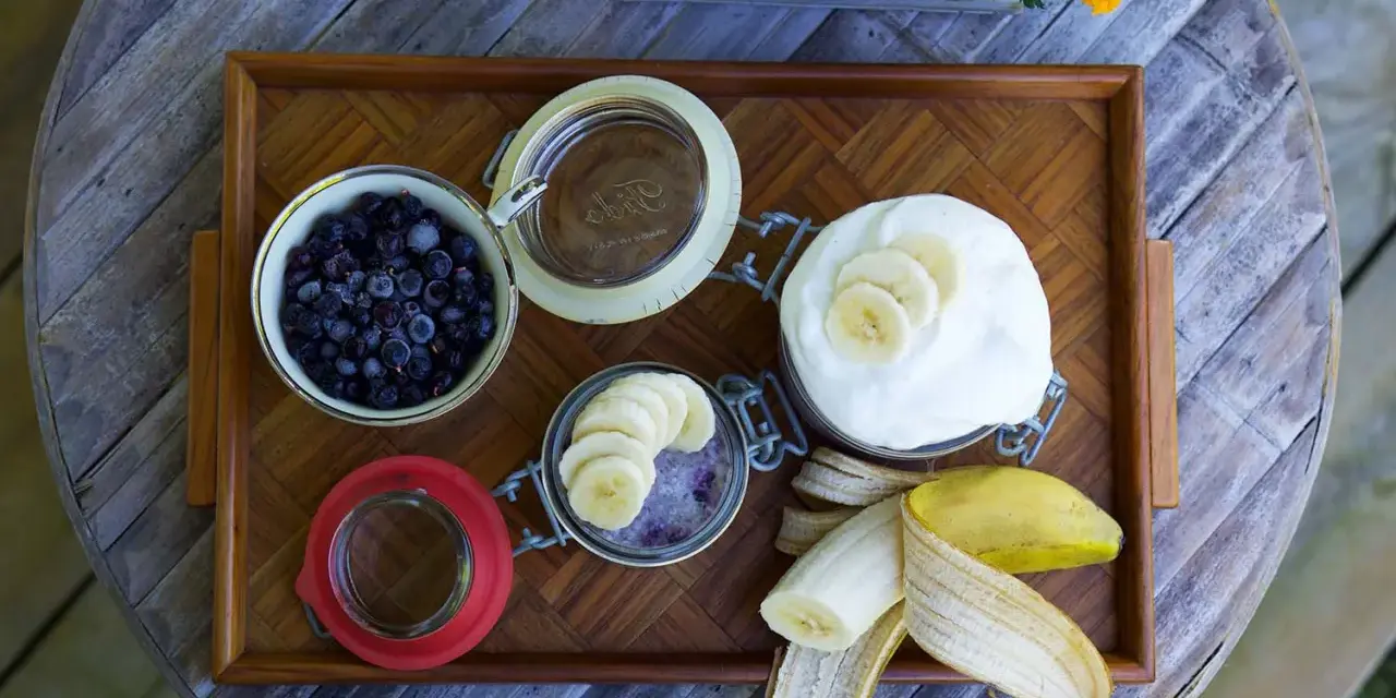 En bricka med ingredienser för sommarmat recept: blåbär, yoghurt, banan och en burk med bär och banan.