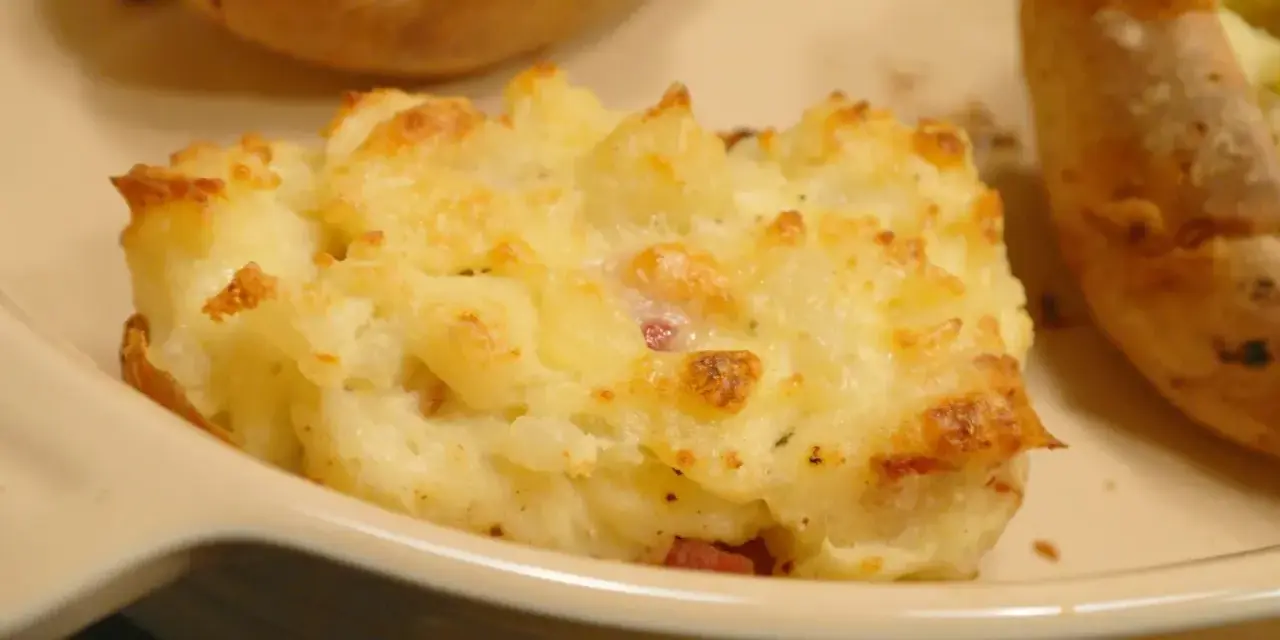 En närbild på en krämig, osttäckt bakad potatis fylld med baconbitar.