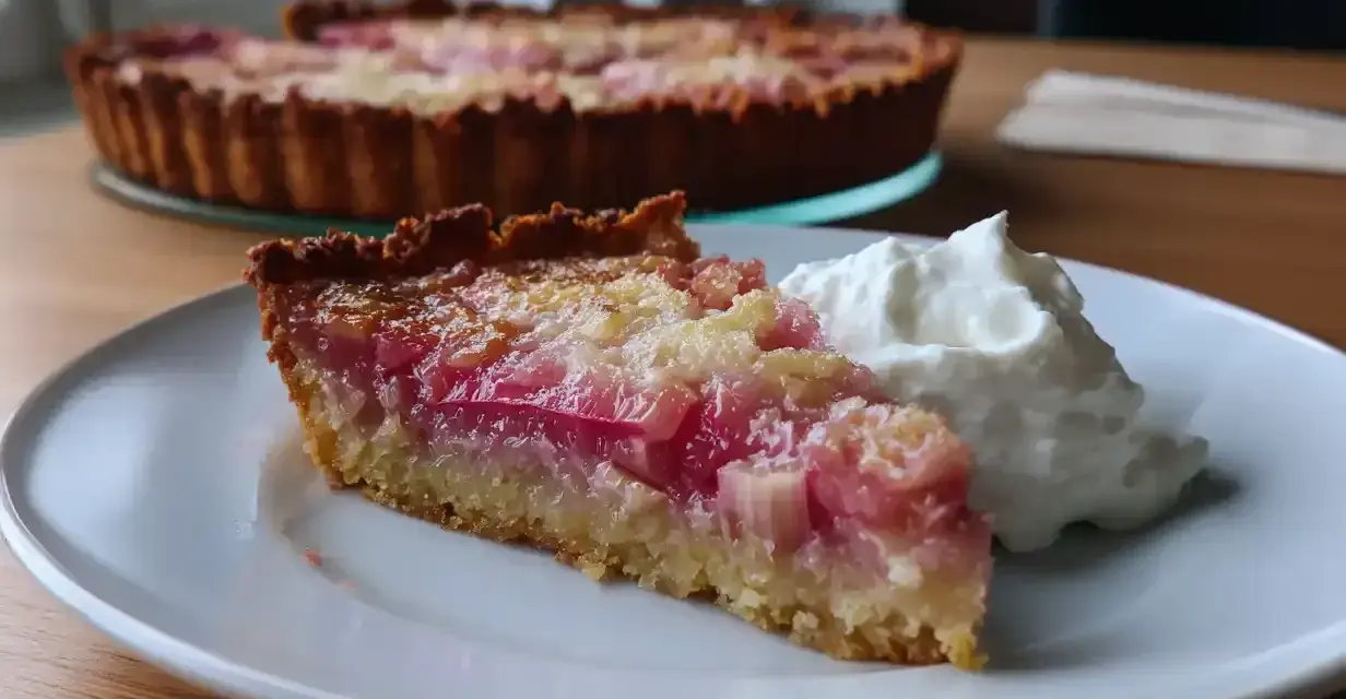 En saftig bit glutenfri rabarberpaj med en klick vispad grädde. Pajen har en gyllene botten och fyllning med rosa rabarberbitar.