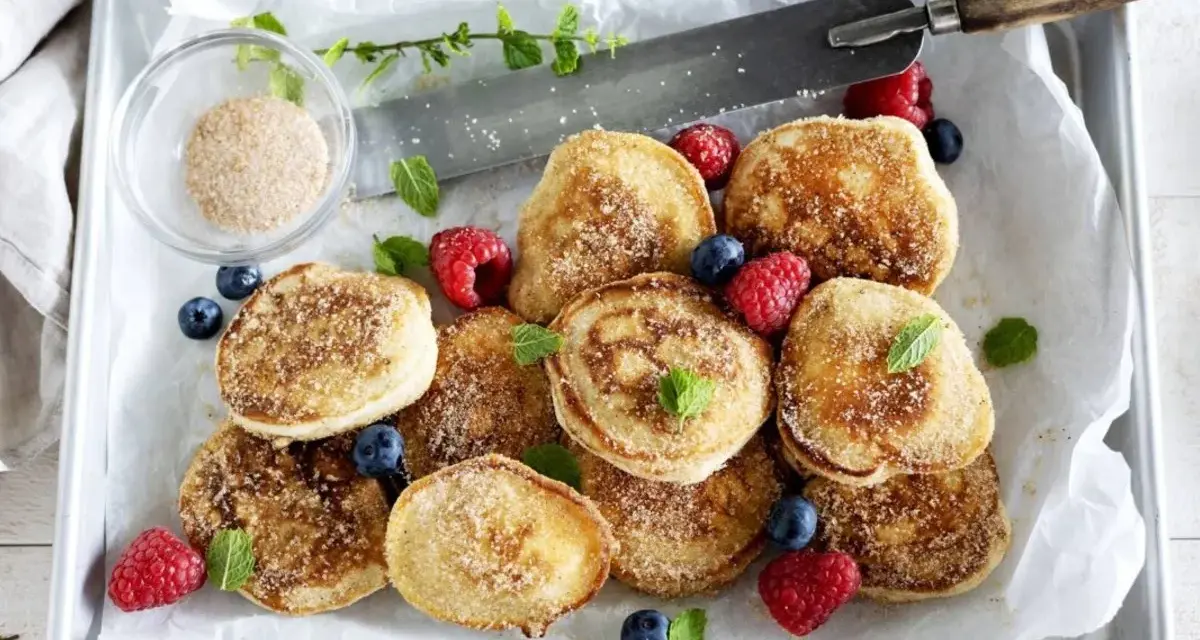 En bricka med nybakade krabbelurer, pudrade med socker och kanel, garnerade med färska bär och mynta. Perfekt för ett krabbelurer recept!
