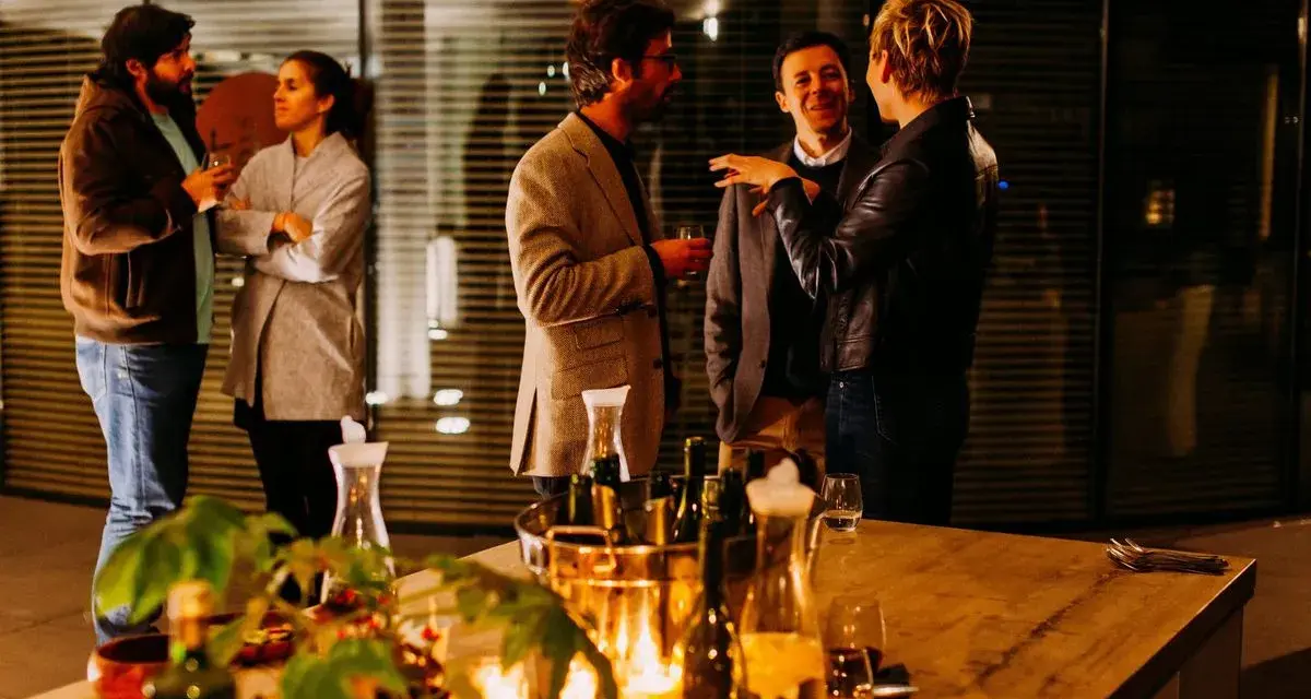 Folk minglar och skrattar under en mysig julfest på jobbet. Ett bord med dryck och ljus skapar stämning.