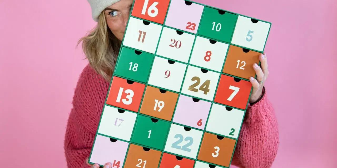 En person med en stickad tröja och mössa håller upp en färgglad julkalender. En perfekt julkalender diy att skapa själv!