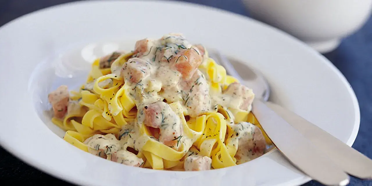 Krämig lax pasta med dill på en vit tallrik. En härlig rätt som passar perfekt för en mysig middag.
