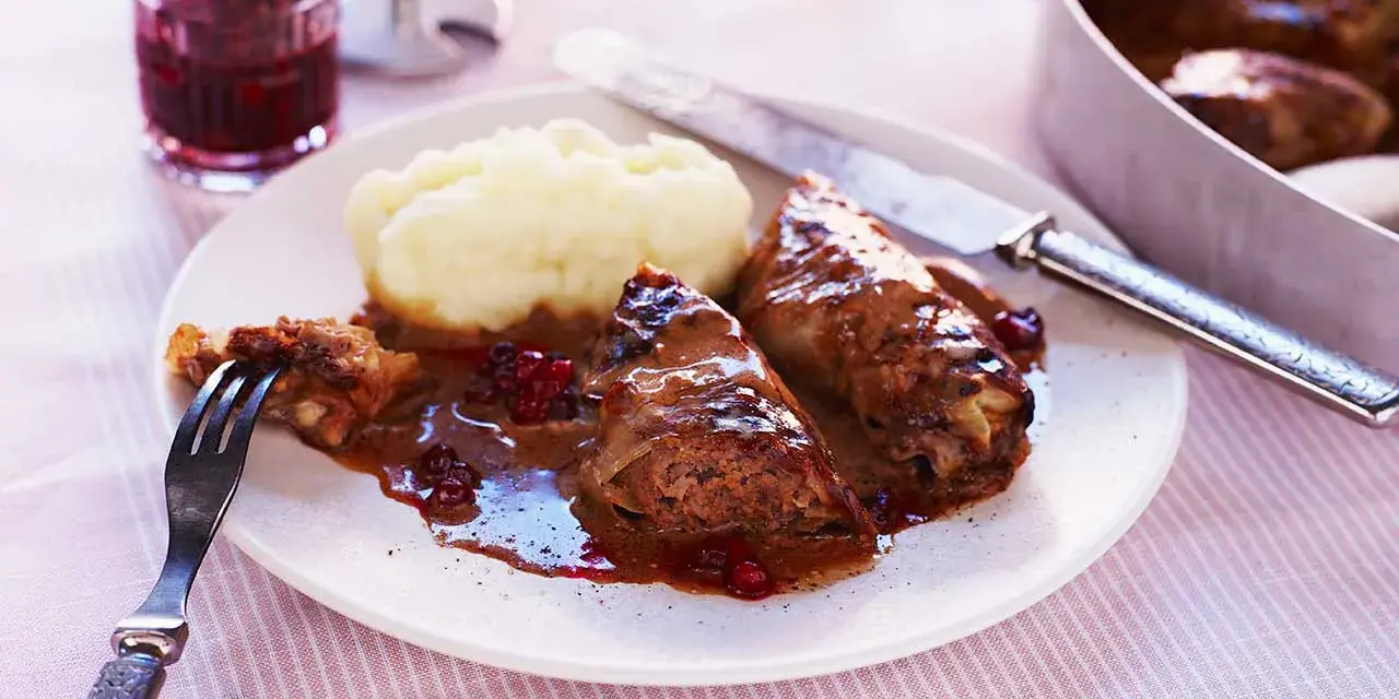 Kåldolmar recept: två saftiga kåldolmar med potatismos och lingonsylt, serverade med en mustig sås.