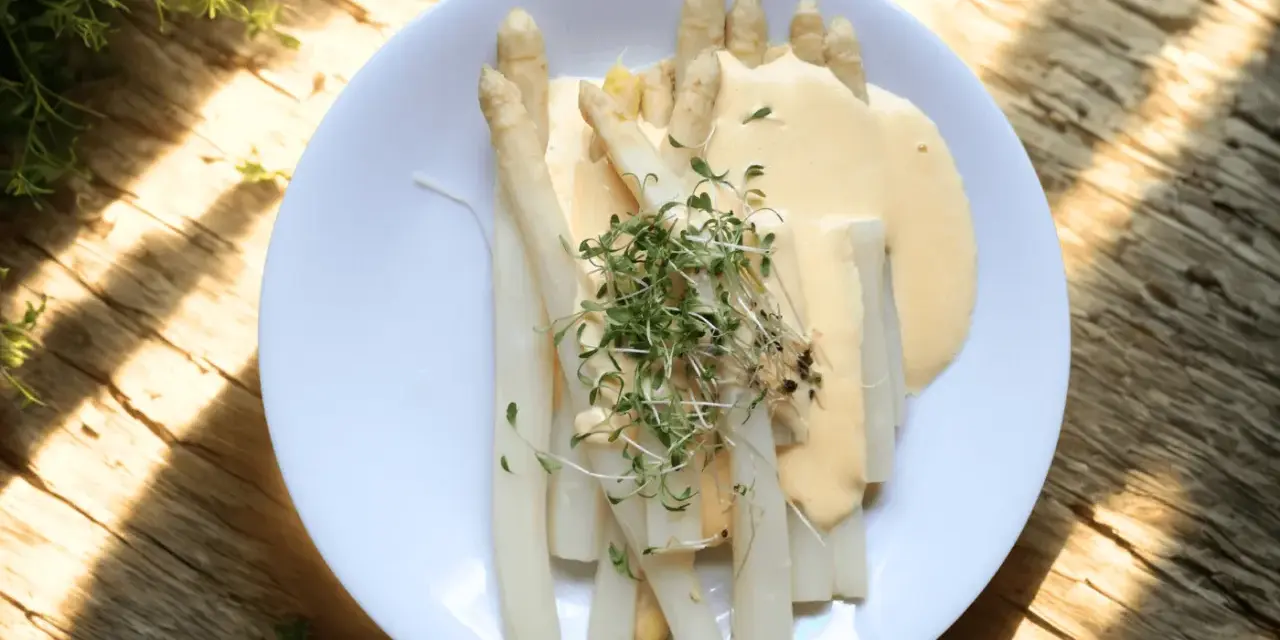 En tallrik med vit sparris, täckt av en krämig sås och toppad med färska groddar. En klassisk svensk vårrätt.