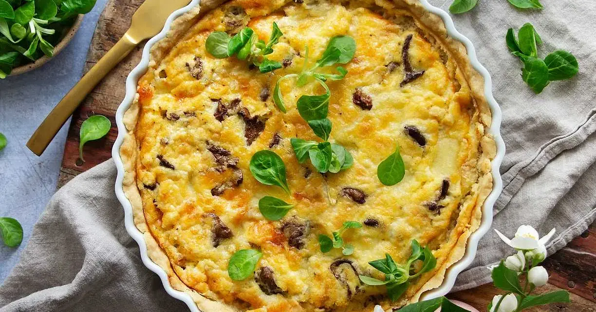 En gyllene kantarellpaj, perfekt för ett höstligt kantarellpaj recept. Garnerad med färska gröna blad och serverad med en gyllene kniv.