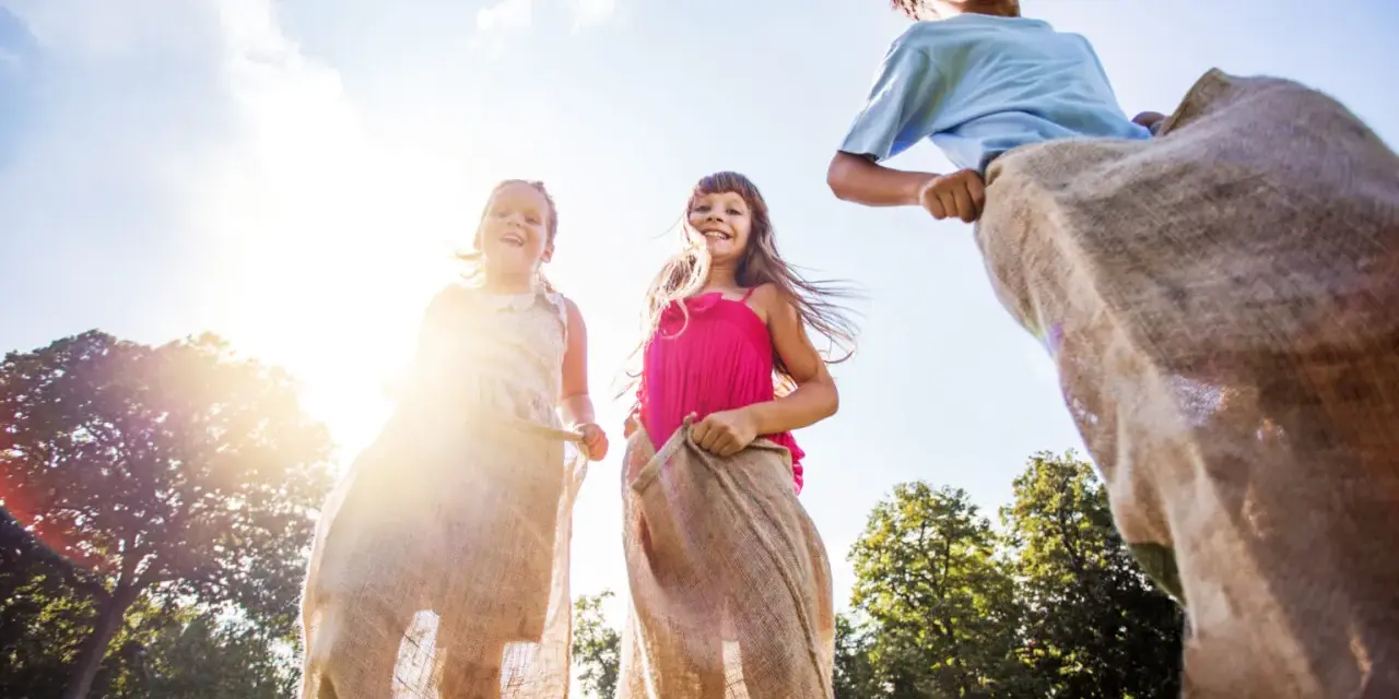 Barn hoppar säcklöpning i solsken, en klassisk midsommaraktivitet. En del av en femkamp midsommar.