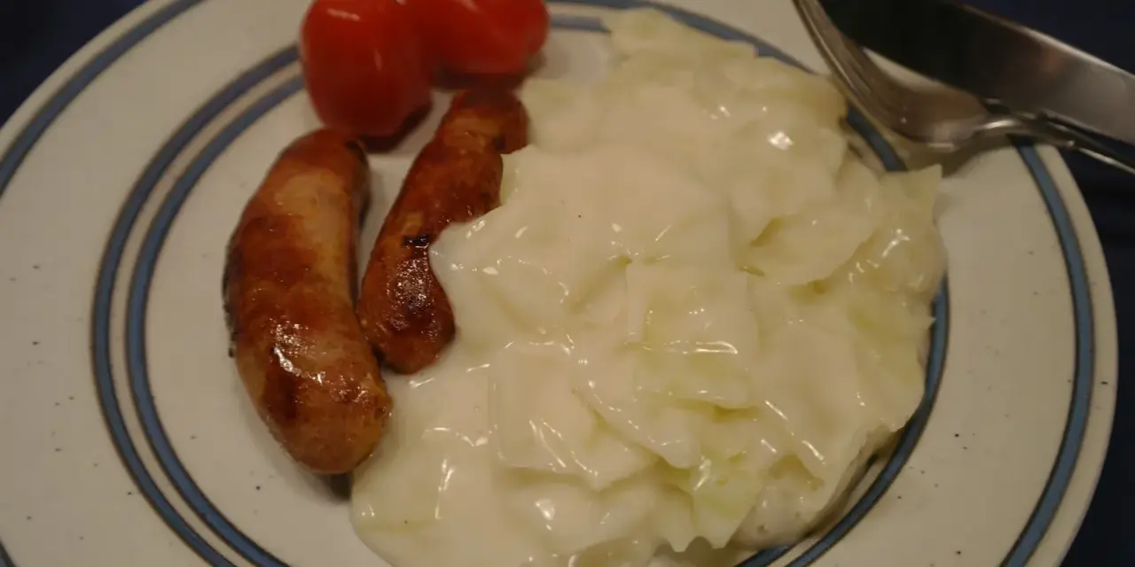 Tallrik med stuvad vitkål, två korvar och körsbärstomater. En klassisk svensk husmanskosträtt.