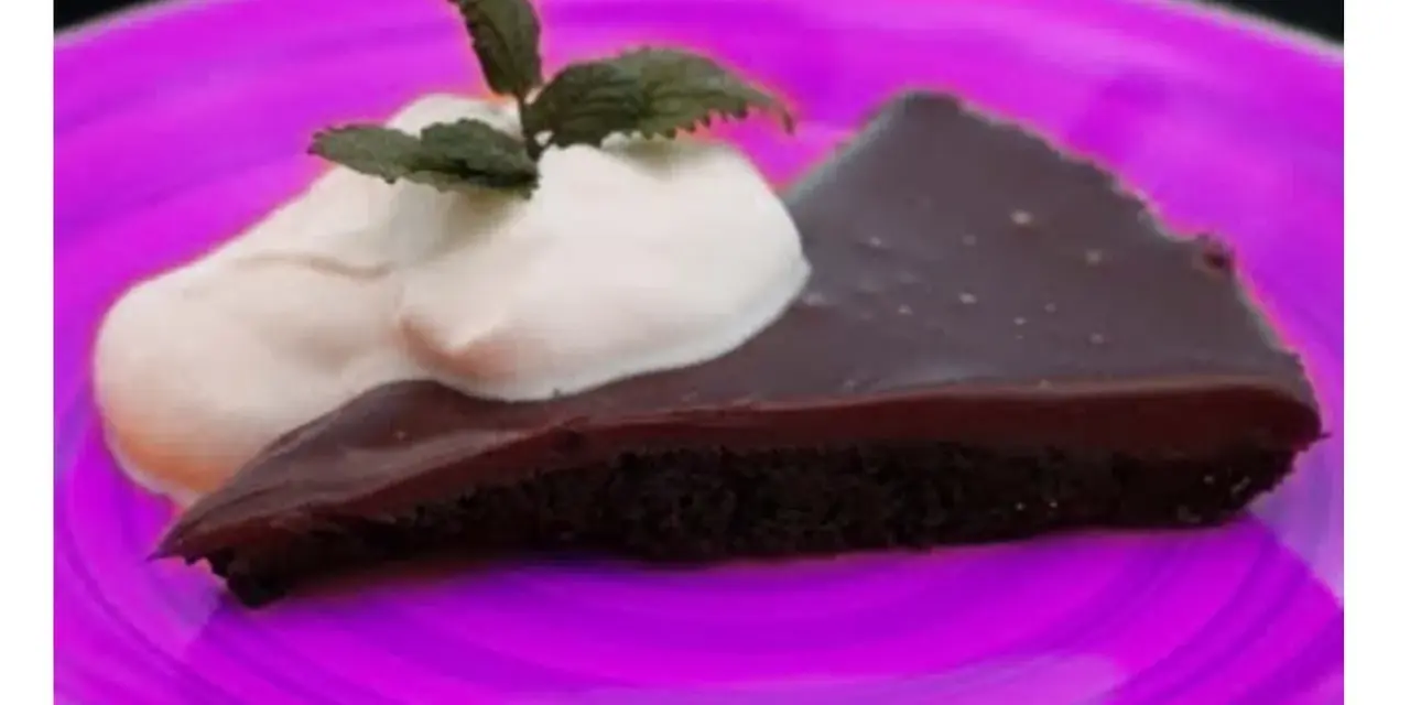 En bit kladdkaka med vispgrädde och mynta på en lila tallrik. Perfekt för en kladdkaka dag!