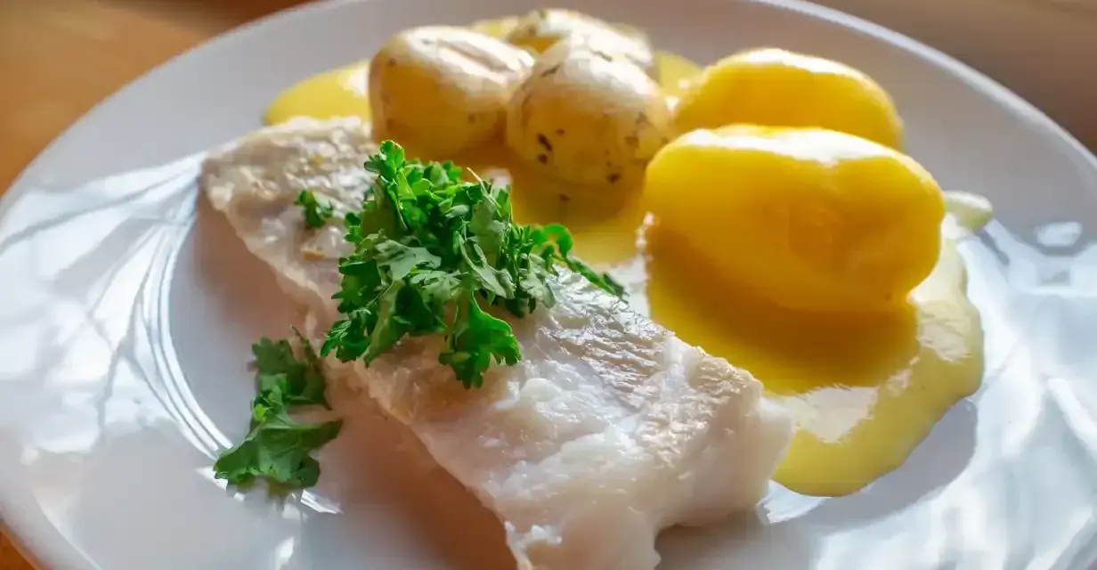 En portion rimmad torsk med kokt potatis och en krämig sås, garnerad med färsk persilja.