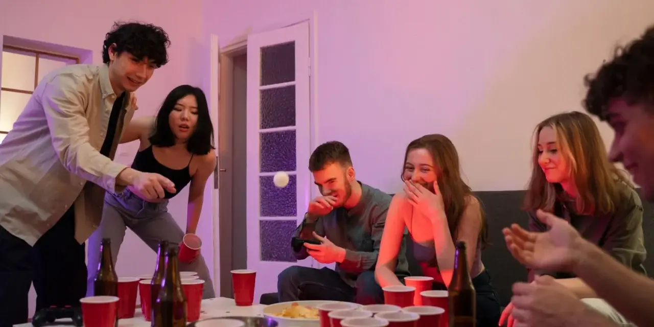 Unga vänner spelar beer pong, en rolig aktivitet med röda muggar och skratt.