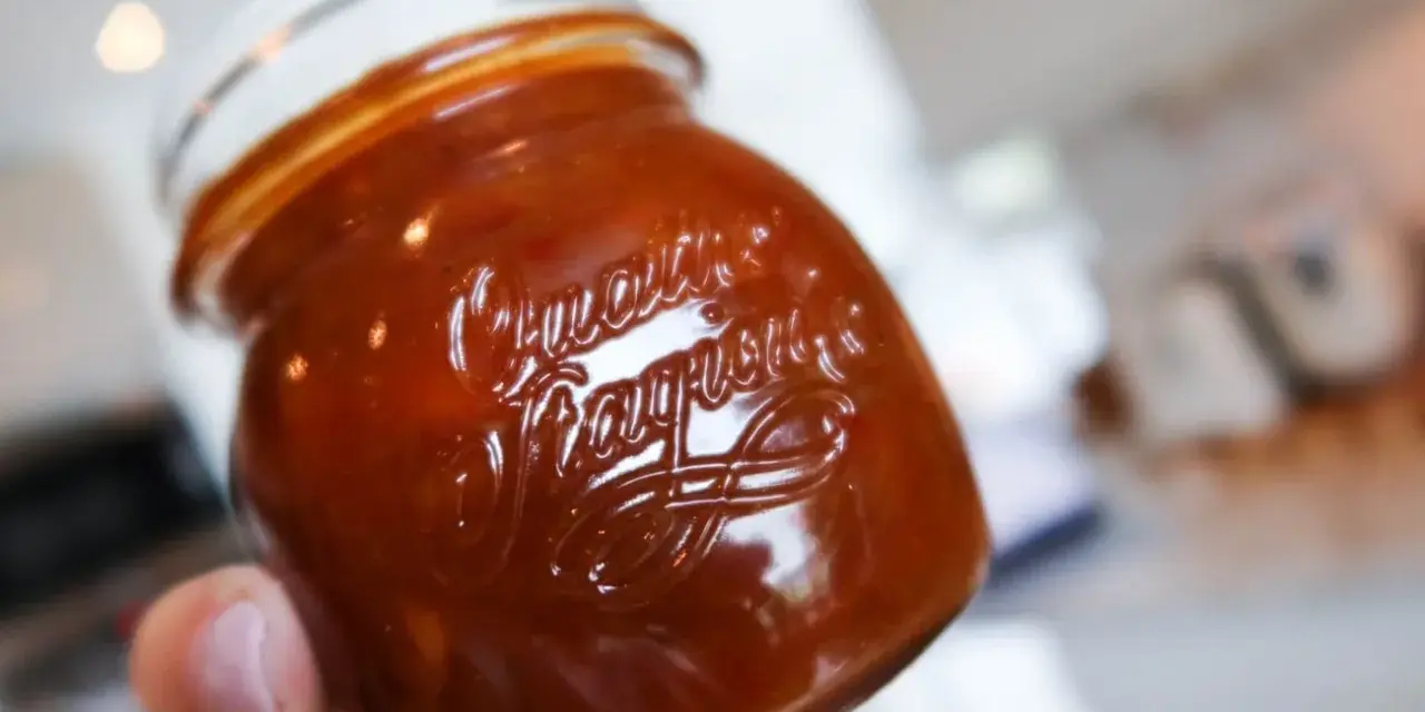 En hand håller ett glas med en mörkröd rabarber chutney.