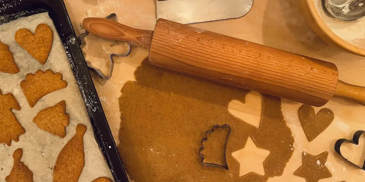 Pepparkaksdeg recept förbereds med kavel och pepparkaksformar. Färdiga pepparkakor ligger på en plåt.