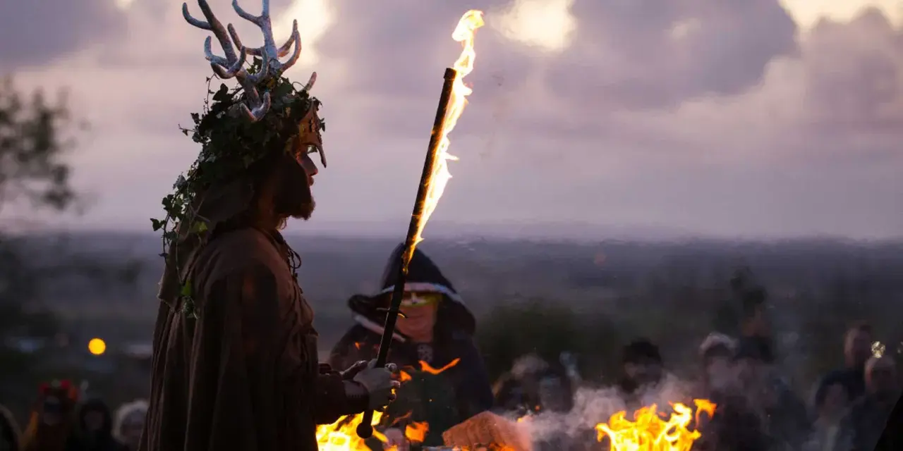 En person med hjorthorn och lövverk håller en fackla vid en eld. En mystisk stämning under halloween i Irland.
