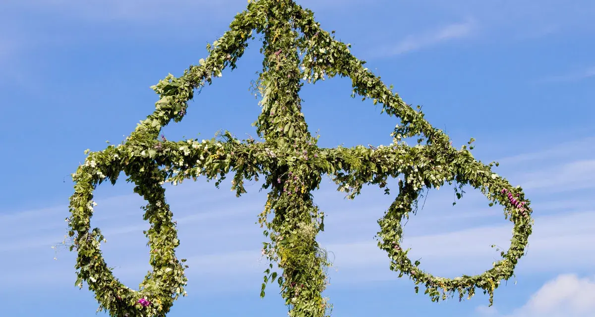 En midsommarstång, dekorerad med grönska och blommor, mot en blå himmel. En symbol för sommar och glädje, en viktig del av fakta om midsommar.