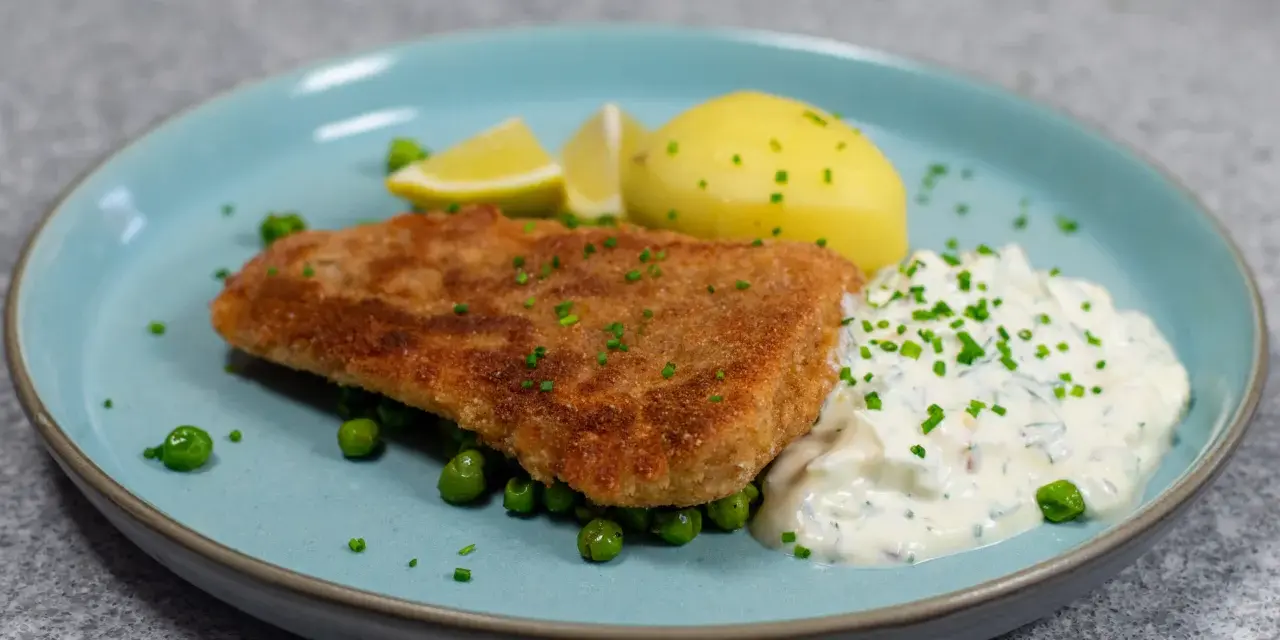 Panerad fisk med kokt potatis, ärtor och en krämig kall sås till fisk, garnerad med gräslök och citronklyftor.