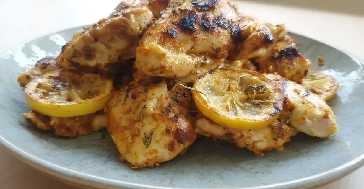 Grillad, saftig marinad kyckling med citronskivor på en ljusblå tallrik. Perfekt för en sommarfest!