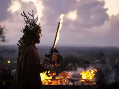 En person med hjorthorn och lövverk håller en fackla vid en eld. En mystisk stämning under halloween i Irland.