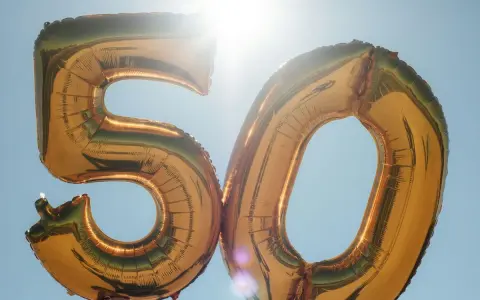 Gyllene ballonger formar siffran 50 mot en klarblå himmel. Perfekt för roliga frågor till 50 års fest!