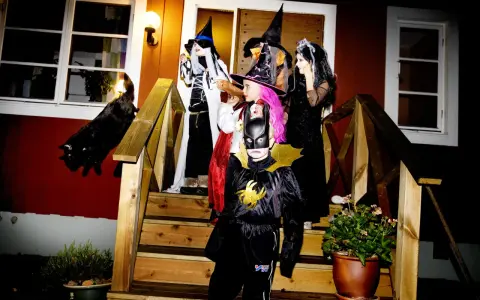 Barn utklädda till häxor och Batman förbereder sig för halloween helg. En svart katt smyger på trappan.
